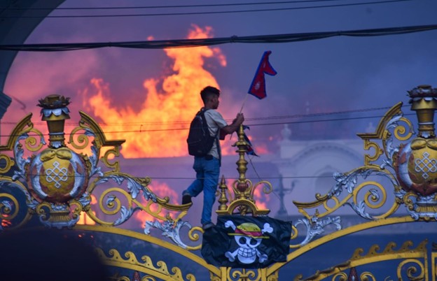 A protester carrying a Nepalese flag hangs a pirate flag as smoke and flames rise from the Singha Durbar, the seat of Nepal’s government, in Kathmandu, Nepal, on September 9, 2025.